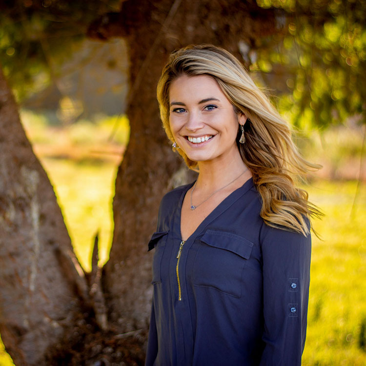 A smiling person standing in front of a tree