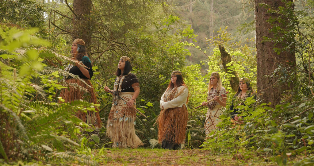 5 women in traditional native dress walk through the forest