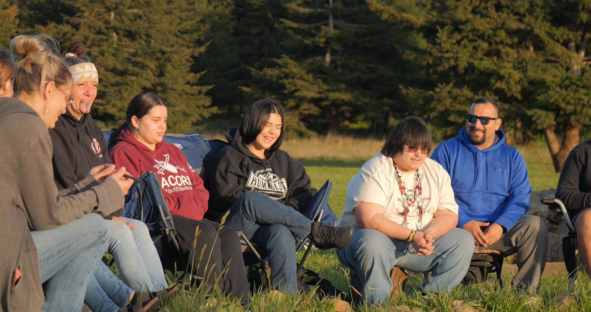 A group of adults and young adults sit in a group and laugh together