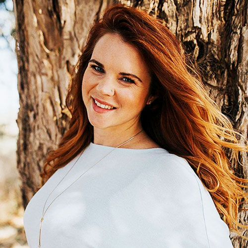 A person stands next to a tree and smiles