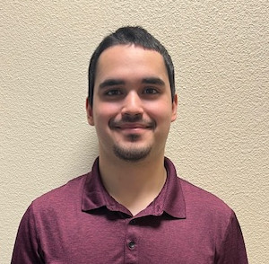A person in a polo shirt stands against a wall and smiles