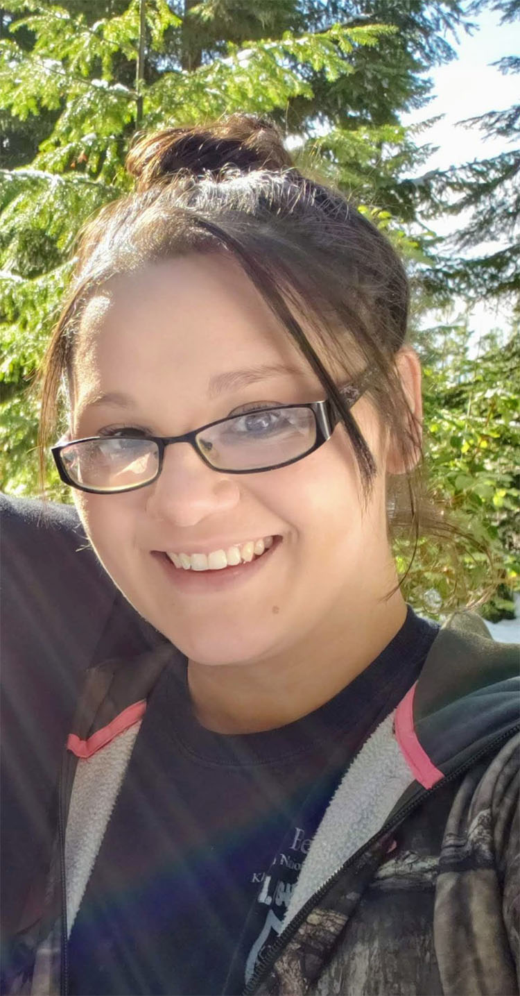 A person stands in front of a tree and smiles