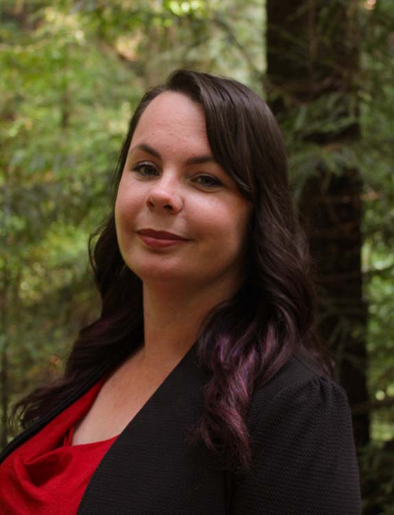 A smiling person stands in front of a tree
