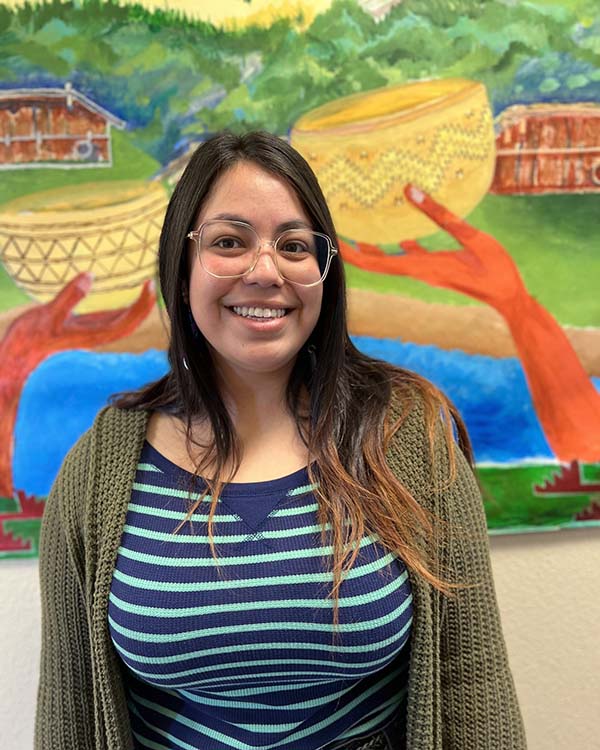 A smiling person stands in front of a mural