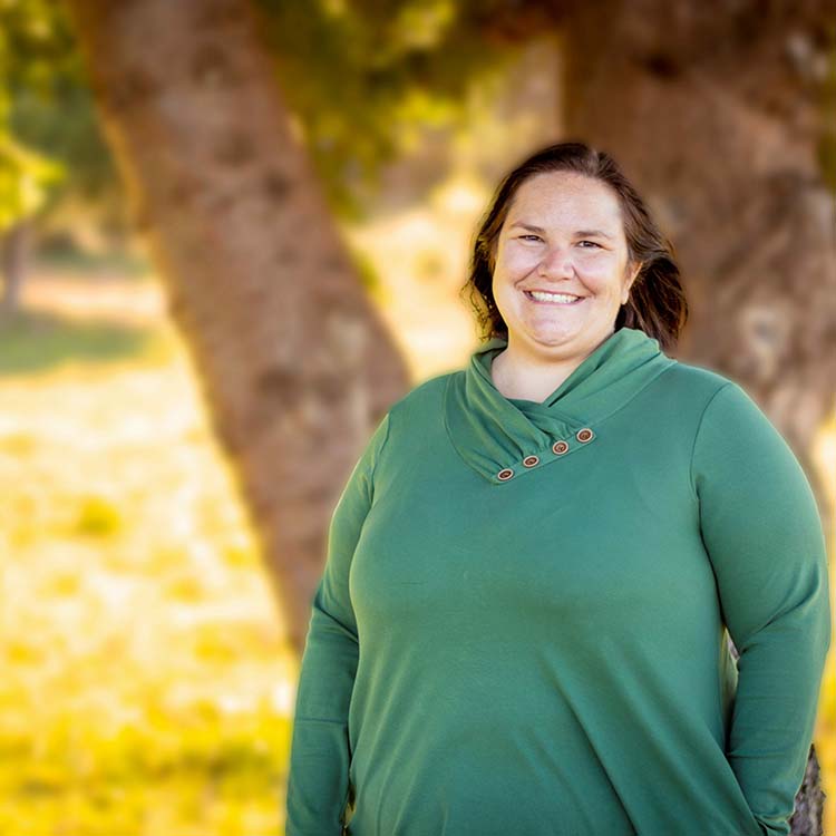 A smiling person stands in front of a tree