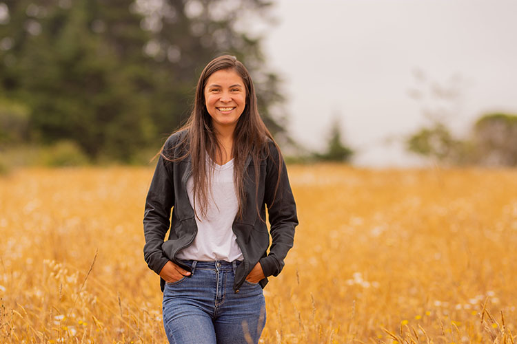 A smiling person stands in a field of flowers