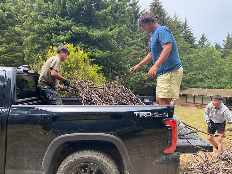 Three young men unload wood from the bed of a pickup