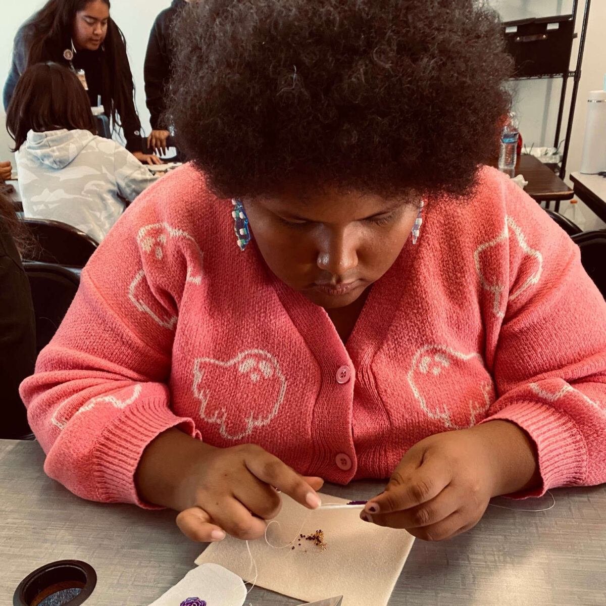 A young adult works on a beading project at a table