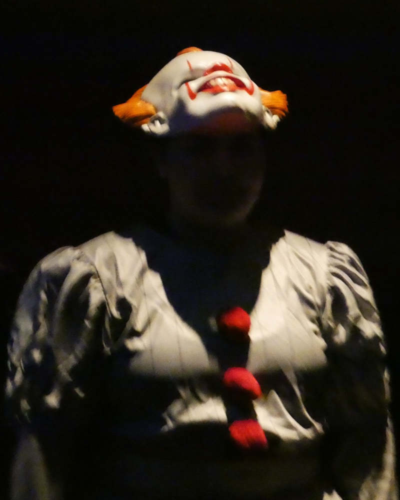 A person wearing a costume of the clown from IT looks up at a sharp light source