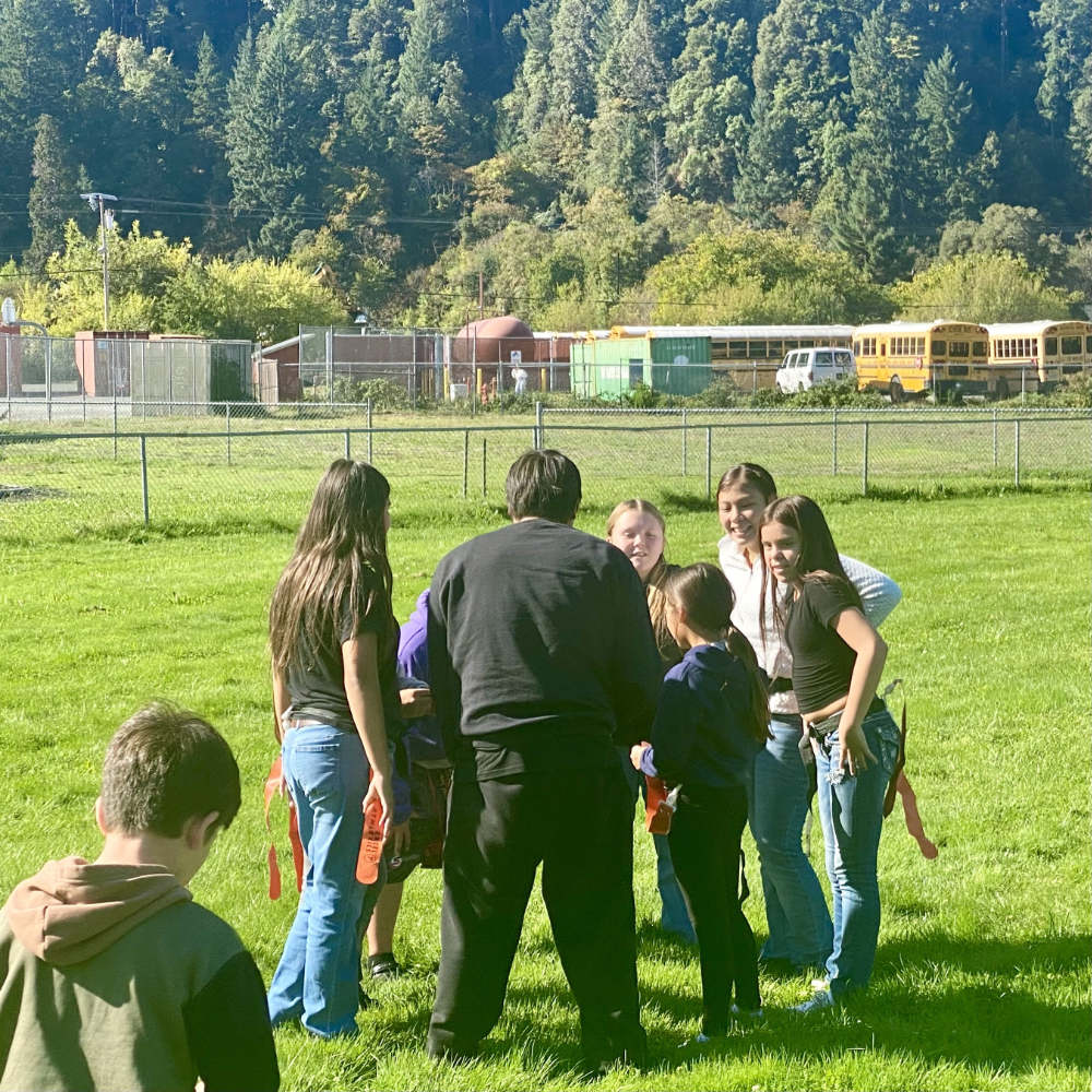 A group of adults and youth huddle together in a field