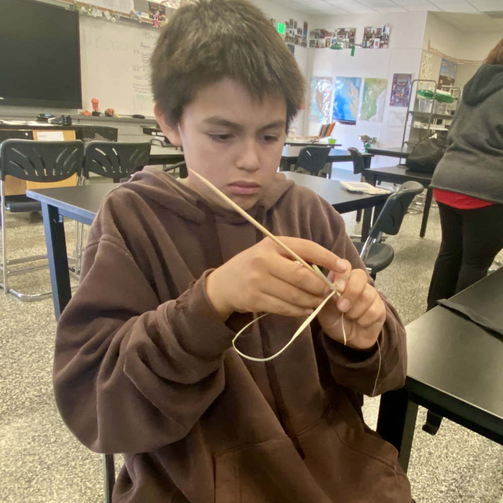A young person weaves something in a classroom