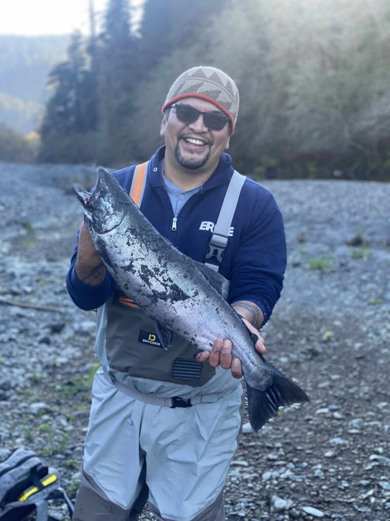 A smiling Native American man holds up a fish