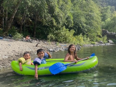 Three children sit in an inflatable raft in the water and smile for the camera