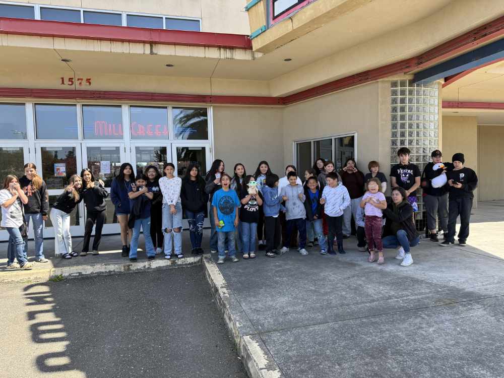 A group of youth and adults pose in front of a movie theater