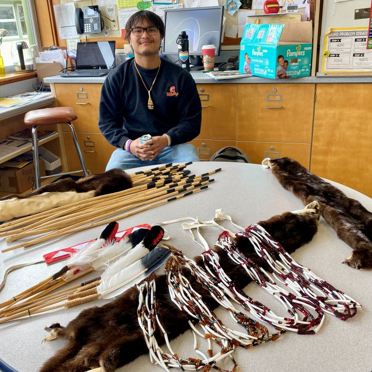 A young Native man next to a display of Native regalia