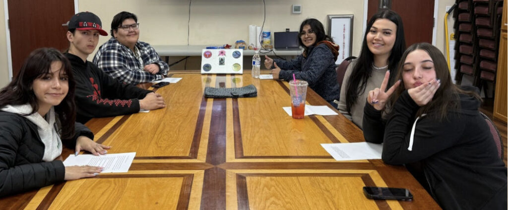 Several young people sit at a boardroom table and smile for the camera