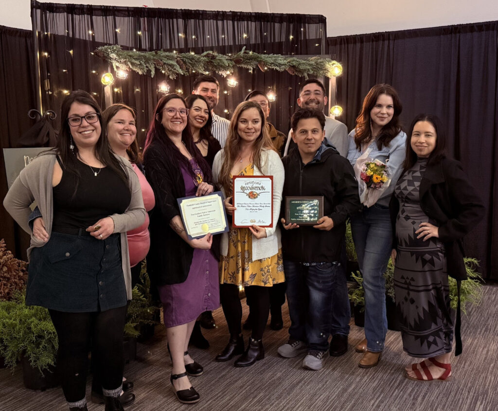 A group of smiling people stand together and hold awards